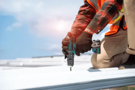 Construction worker using power drill on rooftop wearing safety gear and gloves