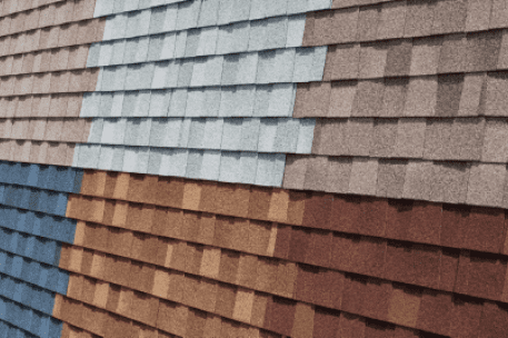 Colorful asphalt roof shingles display in multiple rows showing gray, brown, blue and red samples
