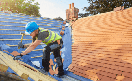 Roofer in safety gear installing clay tiles on residential roof construction project