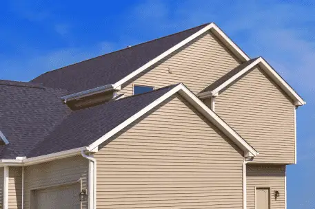 Modern beige vinyl siding house with dark gray asphalt shingle roof against blue sky