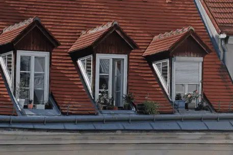 Three dormer windows on red tile roof with potted plants and small balconies