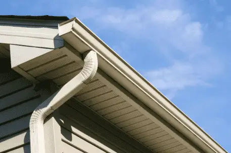 White vinyl gutters and downspout installed on house exterior against blue sky