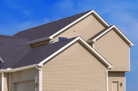 Modern beige vinyl siding house with dark gray asphalt shingle roof against blue sky