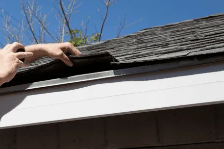 Hand inspecting damaged roof shingles and gutter for home maintenance repair