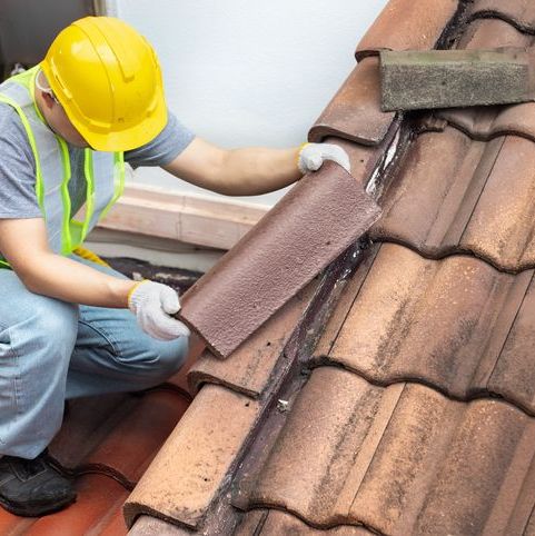 Worker repairing roof tiles with precise placement technique.