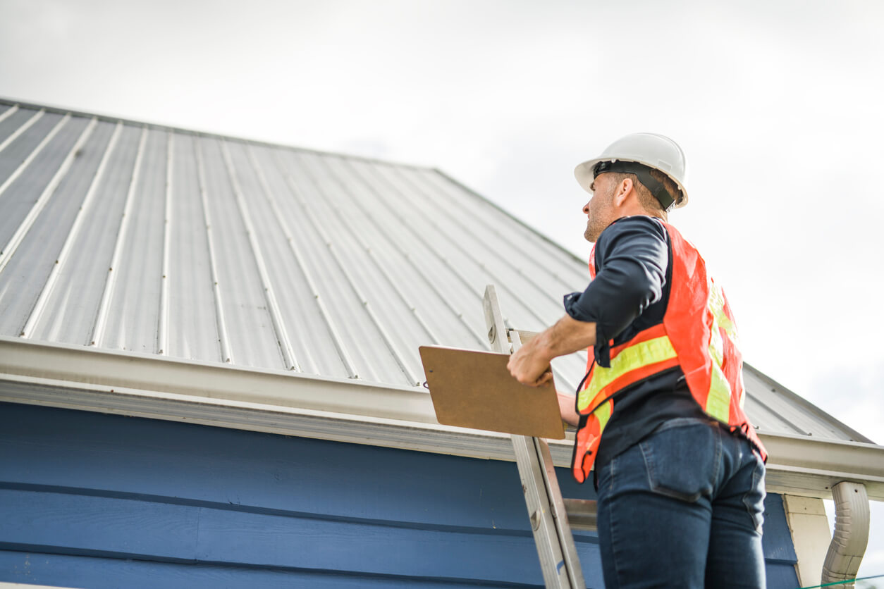 Inspector climbing ladder for roof inspection on a blue building