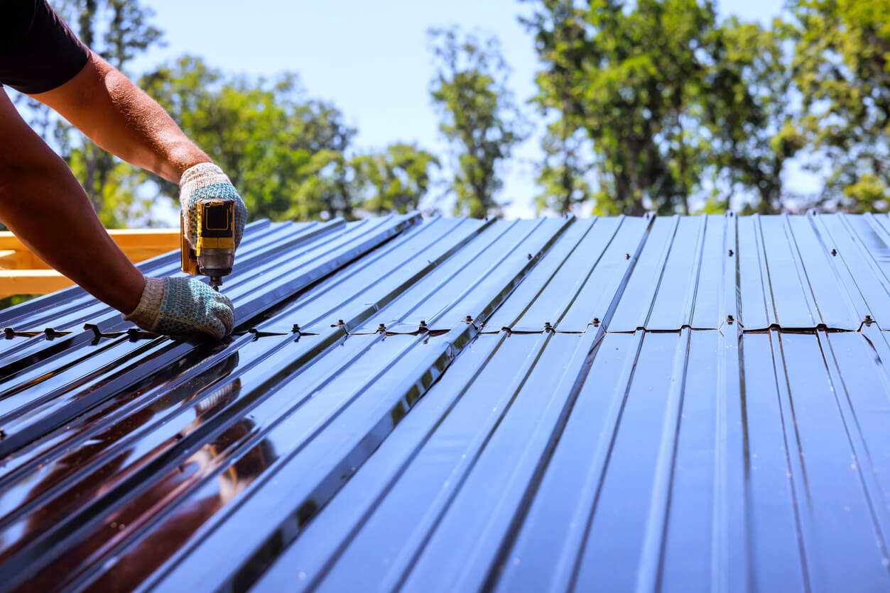 Worker installing metal roof with a drill on a sunny day.